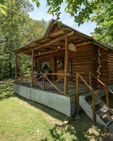 Log cabin with covered porch surrounded by trees at Spring Hill Farm, Rudy, AR